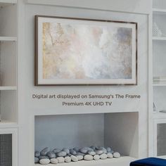 a white fireplace with rocks under it and a painting on the wall above it that says digital art displayed on samsung's the frame