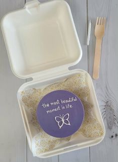 a purple and white box with some food in it next to a fork and spoon