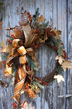 a wreath is hanging on the side of a wooden door decorated with autumn leaves and pine cones