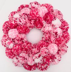 a pink and white wreath with pom - poms hanging from it's center