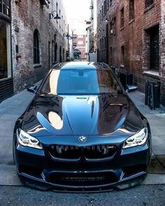 a black car parked on the side of a street next to a brick wall and sidewalk