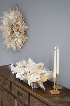 two candles are sitting on top of an old dresser next to a dried flower arrangement