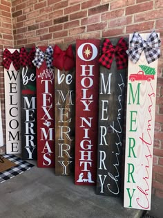 christmas signs are lined up in front of a brick wall with red and white bows