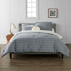 a bed with grey and white striped comforter in a room next to a window