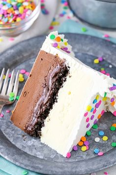 a slice of chocolate cake with white frosting and sprinkles on a plate