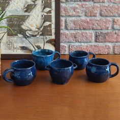 four blue mugs sitting on top of a wooden table next to a vase with a plant in it