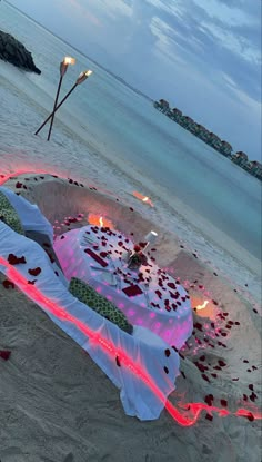 a table set up on the beach with candles and rose petals in front of it