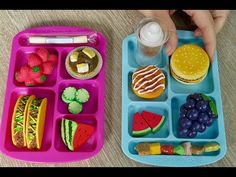 two plastic trays filled with food on top of a wooden table next to a child's hand