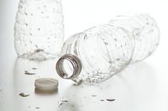 two empty water bottles sitting next to each other on a white surface with drops of water all around them