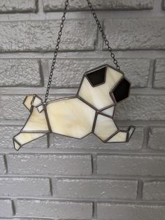 a stained glass dog hanging from a chain on a brick wall in front of a gray brick wall