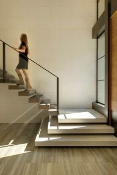 a woman is walking down some stairs in a room with white walls and wood floors