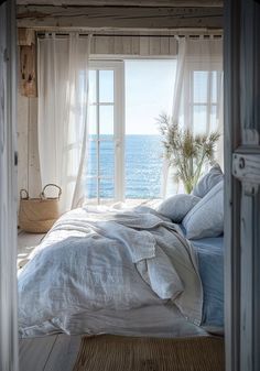 a bed with white sheets and pillows in front of an open window overlooking the ocean