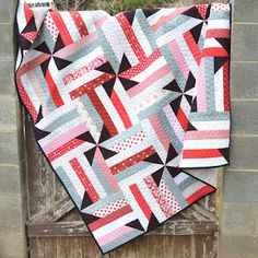 a red, white and black quilt hanging on a wooden door with a brick wall in the background