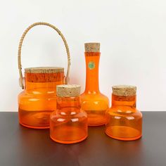 an assortment of orange glass bottles with cork tops and lids on a wooden table next to a basket