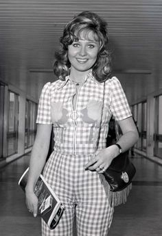 an old photo of a woman in plaid overalls holding a purse and smiling at the camera