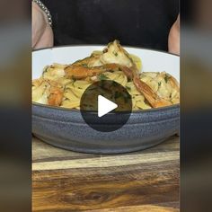 a bowl filled with pasta and shrimp on top of a wooden table next to a person