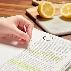 a person writing on top of an open book with lemons in the back ground