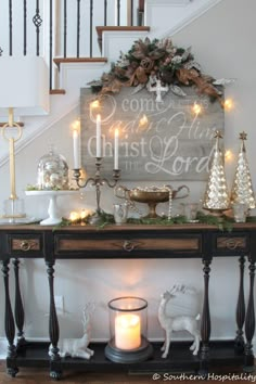 a table with christmas decorations and candles on it in front of a staircase case that says come to the christmas lights at the bottom