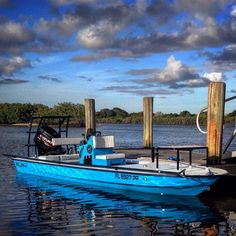 a small blue boat docked at a pier on the water with clouds in the sky