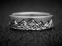 a silver ring with mountains on it sitting on top of a carpeted floor in front of a black background