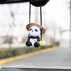 a stuffed panda bear hanging from the side of a car window with a hat on