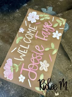 a welcome home sign made out of brown paper with pink and white flowers on it