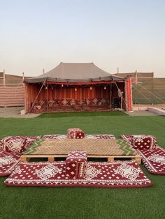 a large tent set up with red and white rugs on the grass in front of it