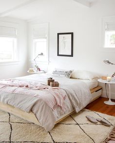 a bedroom with white walls and flooring has a bed made up in pink linens