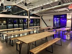 an empty room with tables and benches in front of large glass windows at night time