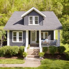 a small gray house with white trim and windows on the front porch, surrounded by trees