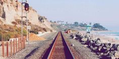 a train track next to the beach with people walking on it and in the background