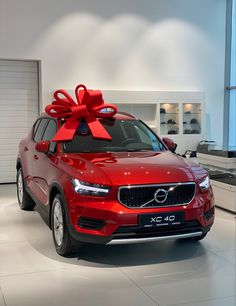 a red volvo car with a large bow on the hood in a showroom area