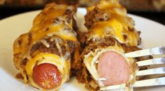 a white plate topped with two stuffed hot dogs covered in cheese and sauce next to a fork