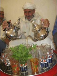 a man pouring water from a pitcher into glasses on top of a tray filled with drinks