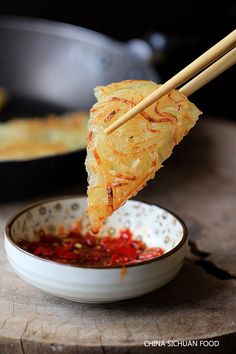 chopsticks holding up food in a bowl with sauce on the table next to it