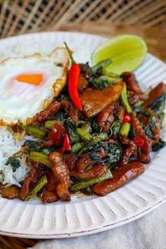 a white plate topped with rice and meat next to an egg on top of it