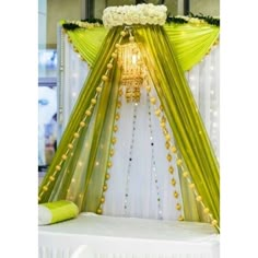 a white and green wedding setup with flowers on the headboard, drapes and lights in the background