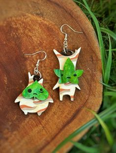 two green and white earrings sitting on top of a piece of wood