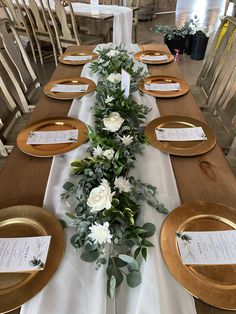 the table is set with gold plates and flowers on it, along with place settings