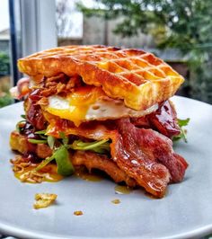 a waffle sandwich with bacon, lettuce and egg on it sitting on a plate