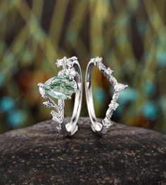 two silver rings with green and white stones on top of a rock in front of some leaves