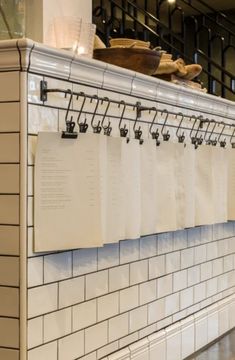 a kitchen with white tile walls and black metal hooks on the wall above it is a menu board that has notes attached to it