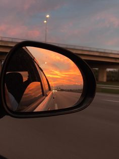 the rear view mirror of a car is shown as the sun sets in the distance