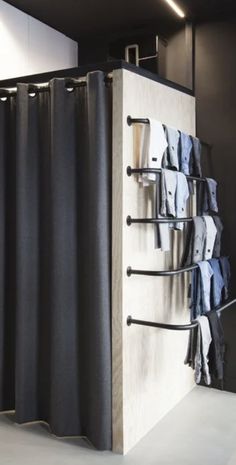 a room with black curtains and clothes hanging on the wall next to a white floor