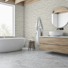 a white bath tub sitting next to a window in a bathroom under a round mirror