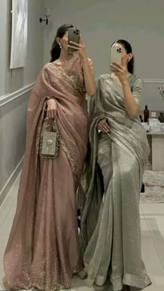 two women in sari taking pictures with their cell phones while standing next to each other