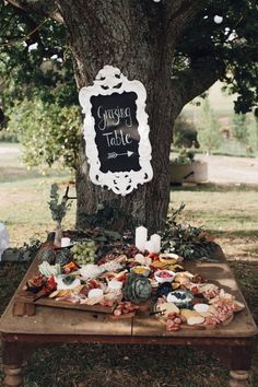 a table topped with food under a tree next to a sign that says guest table