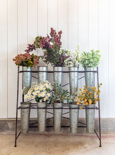 an assortment of potted plants on a metal stand with flowers in them and white walls behind it