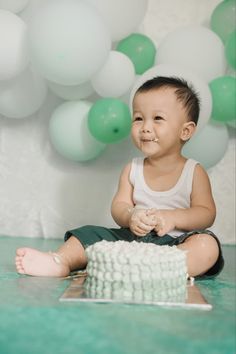 a little boy sitting on the floor in front of a cake with white frosting