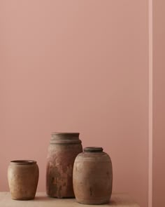 three vases sitting on top of a wooden table next to a light pink wall